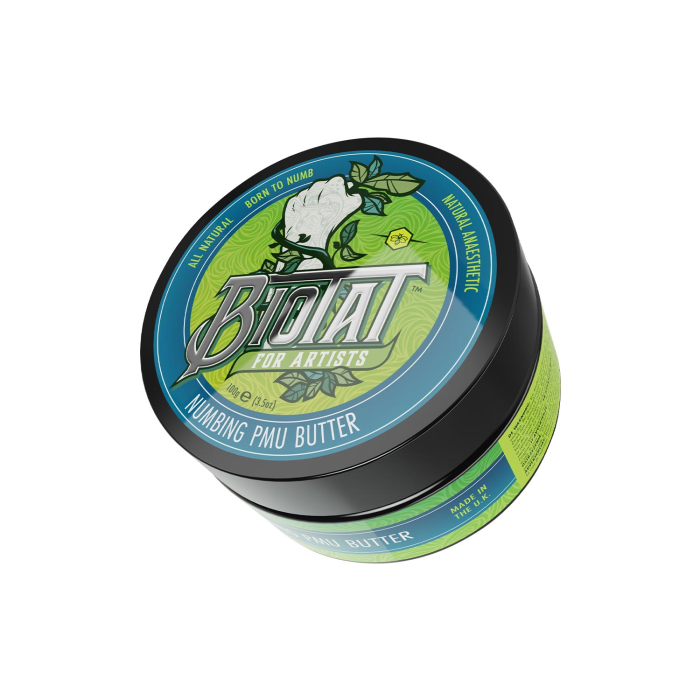 Une boîte ronde de Beurre PMU anesthésiant BIOTAT 100 g, pour artistes, avec un couvercle décoré d’une rose blanche et de motifs verts, bleus et noirs, accompagnés des textes « Born to numb » et « Numbing PMU Butter ».